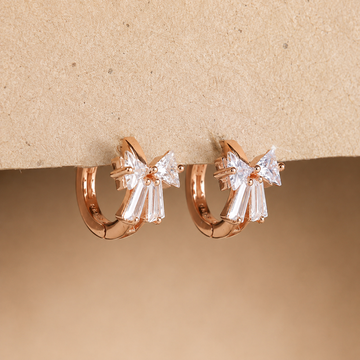 Rose gold hoop earrings with clear gemstones on a beige background